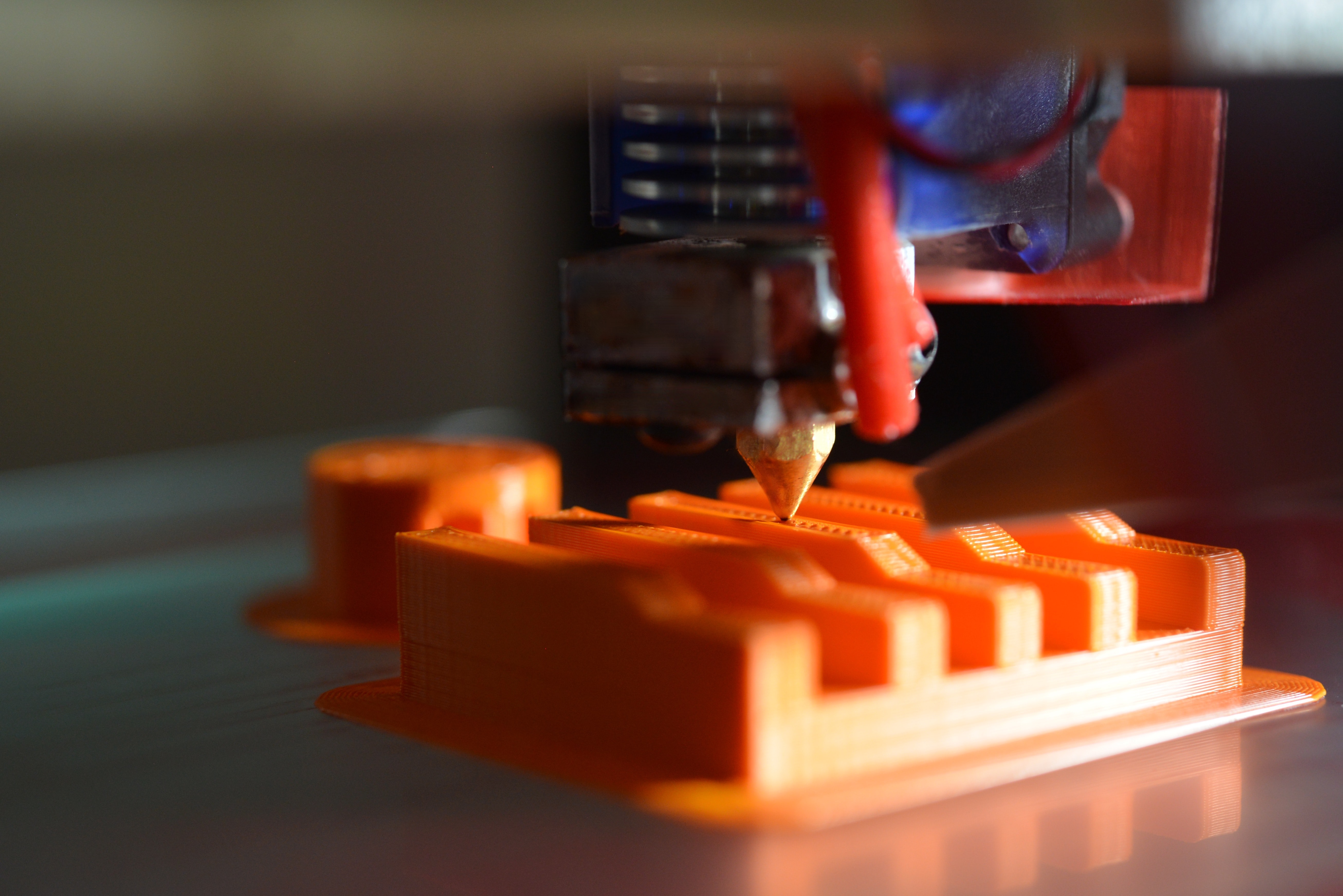 A 3D printer nozzle depositing layers of orange plastic