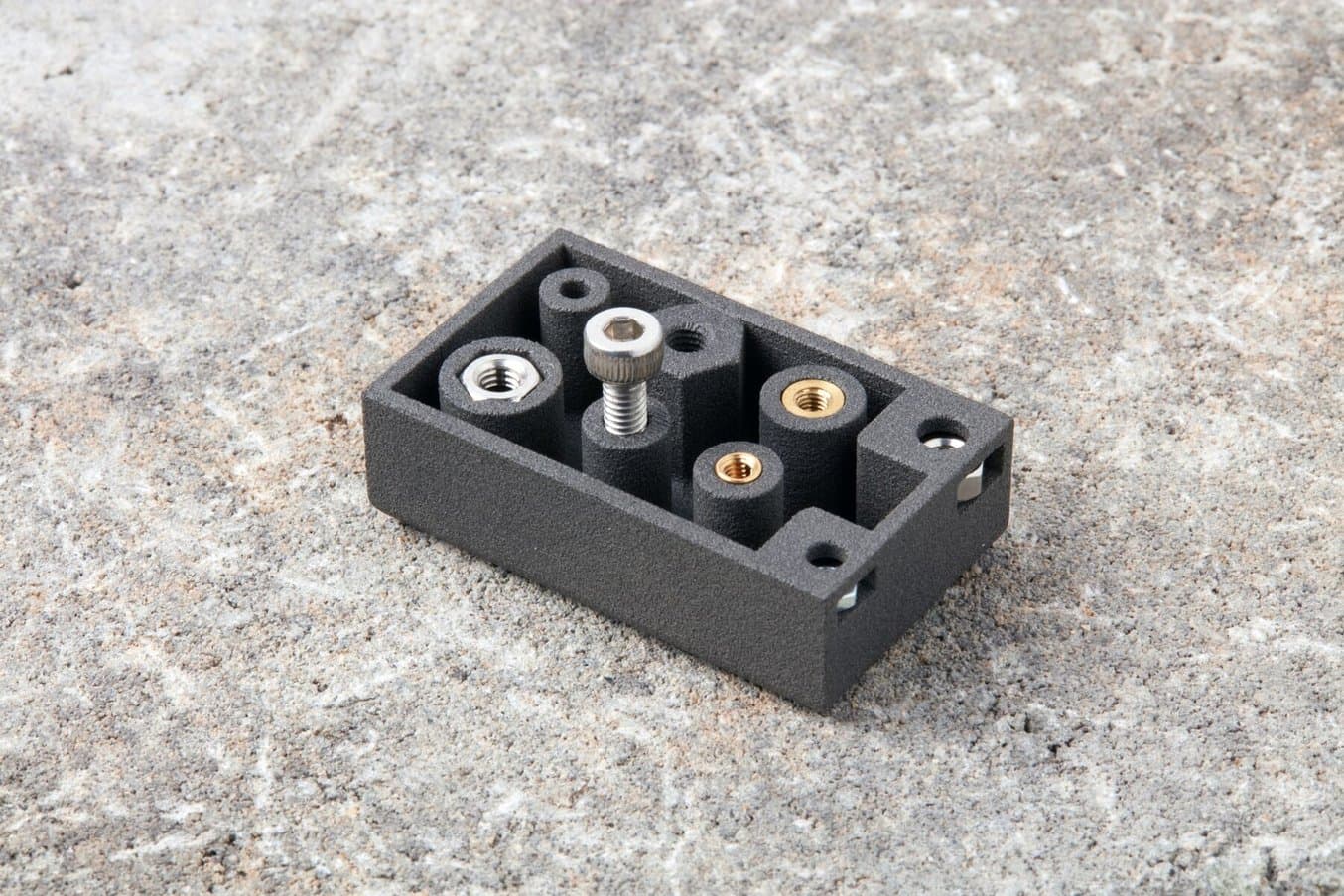 Printed demonstration part containing captive nuts, brass threaded inserts, and screw holes